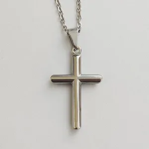 Close-up of minimalist stainless steel cross pendant necklace on textured background.