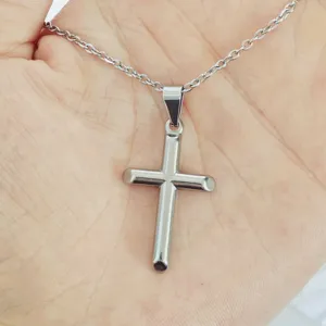 Close-up detail of a minimalist stainless steel cross pendant necklace on a hand.