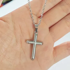 Close-up of a minimalist stainless steel cross pendant necklace held in hand.
