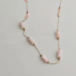 Macro detail of a gold stainless steel chain necklace with pink bamboo-joint beads.