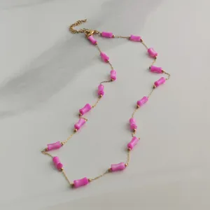 Detail of gold chain necklace with pink bamboo-shaped beads on marble background