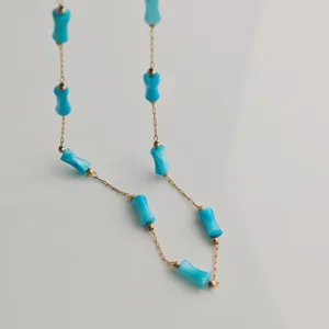 Macro view of bright blue bamboo-shaped beads on a delicate gold stainless steel chain necklace
