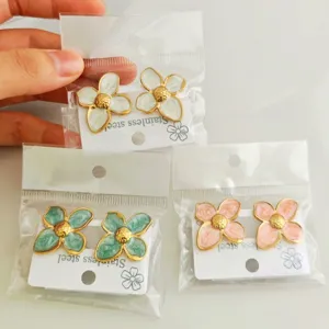 Detailed view of three pairs of colorful enamel flower earrings in their plastic packaging
