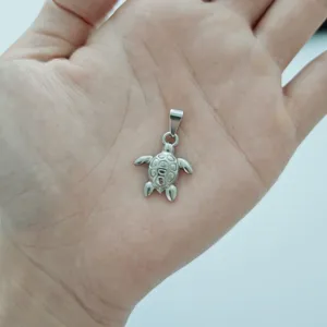 Close-up of a silver stainless steel sea turtle pendant on a human hand for scale