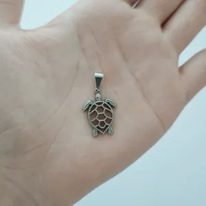 Macro view of a stainless steel sea turtle pendant held in hand for scale demonstration