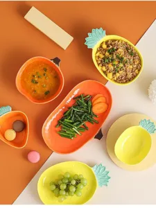 Lifestyle scene showing various fruit-shaped ceramic plates and bowls with fresh food.