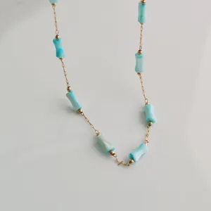 Close-up detail shot of a gold chain necklace featuring turquoise-colored bamboo-shaped beads