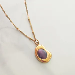 Detailed close-up of a vintage gold-plated necklace with a purple cabochon stone pendant.