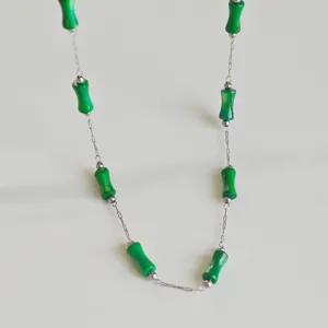 Detailed view of a stylish stainless steel necklace featuring green bamboo-shaped beads