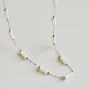 Close-up detail of a minimalist stainless steel chain featuring white bamboo-shaped beads