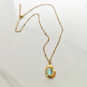 Close-up of elegant gold stainless steel necklace featuring a light blue stone pendant