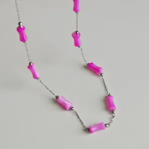 Detail view of vibrant pink bamboo-shaped beads on a slim stainless steel chain necklace.