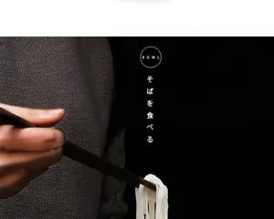 Detailed close-up of wooden chopsticks picking up white noodles for a Japanese ceramic bowl
