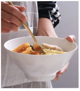 Primo piano di una ciotola in ceramica bianca a forma di cappello con pasta e forchetta d'oro.