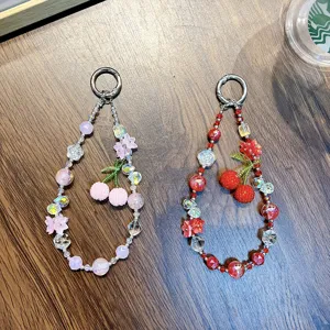 Elegant beaded cherry phone charms in pink and red with crystal accents on a wood table