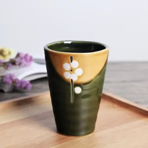 Primer plano de una taza de té matcha japonesa de cerámica con esmalte verde y flores
