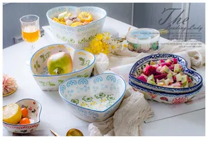 Close-up of heart-shaped ceramic bowls with floral patterns and fresh fruit decorations