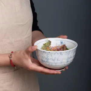 Bol en céramique style japonais avec motif floral bleu tenu par des mains