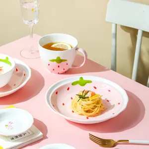 Juego de vajilla de cerámica fresa con plato, bol y taza sobre mesa rosa