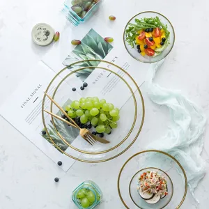 Elegant gold-rimmed glass salad bowls and fruit plates on a white marble tabletop
