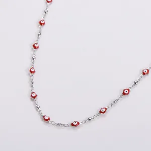 Close-up detail of stainless steel collarbone chain featuring red Hamsa hand and evil eye charms