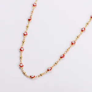Close-up detail of stainless steel gold chain with red Hamsa hand and evil eye charms.
