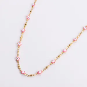 Close-up of a gold stainless steel necklace with pink enamel Hamsa hand charms.