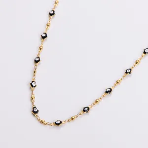Close-up of gold stainless steel Hamsa hand necklace with black enamel evil eye charms.