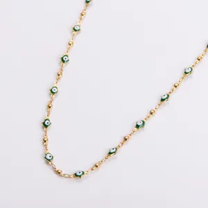 Macro detail of a minimalist gold-toned Hamsa hand necklace with green evil eye charms.
