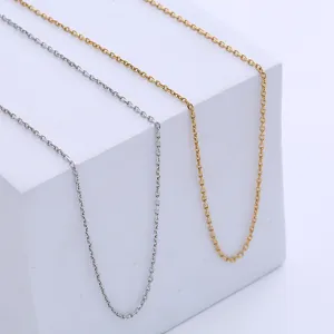 Minimalist faceted cross chains in gold and silver finishes on a white geometric pedestal.