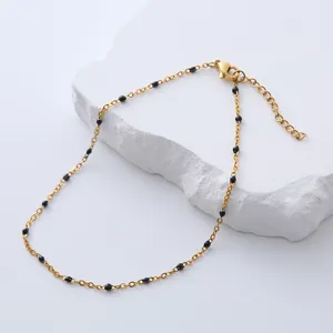 Detalle de tobillera de acero dorado con cuentas de esmalte negro sobre soporte de piedra