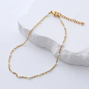 Detalle de cadena de acero inoxidable dorado con cuentas de esmalte blanco sobre piedra