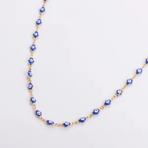 Dettaglio macro della collana in acciaio dorato con ciondoli hamsa evil eye smaltati
