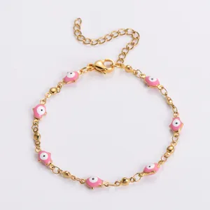 Dettaglio di un bracciale dorato in acciaio con ciondoli in smalto rosa a forma di occhio turco