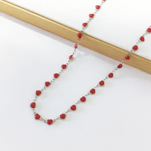 Detail view of a stainless steel necklace with small red enamel heart charms on a silver chain.