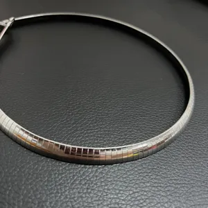 Gros plan d'un collier ras du cou Omega en acier poli sur fond de cuir noir texturé