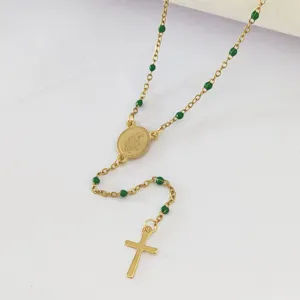 Detail of gold stainless steel religious necklace with green beads and cross pendant.