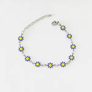 Dettaglio di un bracciale in acciaio inossidabile con piccole margherite blu e gialle.