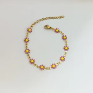 Dettaglio di un braccialetto a catena in oro e acciaio con margherite in smalto rosa e giallo.