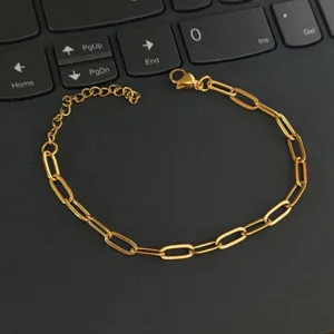 Detailed view of a gold-plated stainless steel paperclip chain bracelet on a black surface.