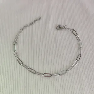Detail view of a silver stainless steel paperclip chain bracelet on ribbed fabric.