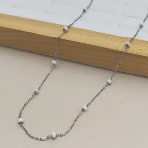 Close-up detail of a minimalist stainless steel necklace with white enamel beads