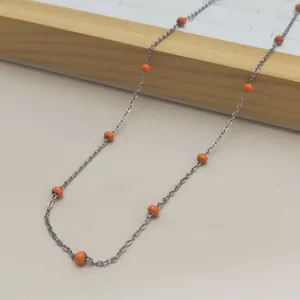 Macro detail of stainless steel necklace chain with vibrant orange enamel beads
