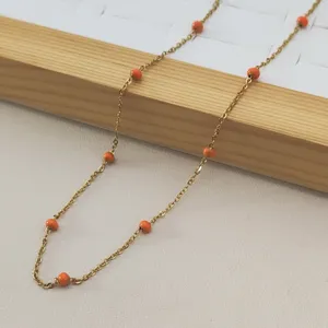 Detailed view of a gold stainless steel necklace with vibrant orange enamel beads.