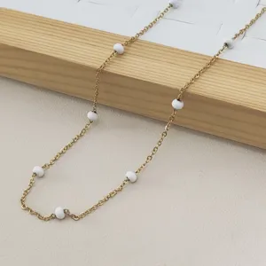 Close-up detail of a gold stainless steel necklace with round white enamel beads.