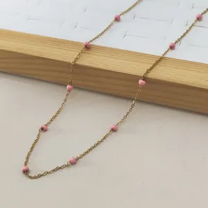 Detailed view of a gold stainless steel necklace with pink enamel bead accents
