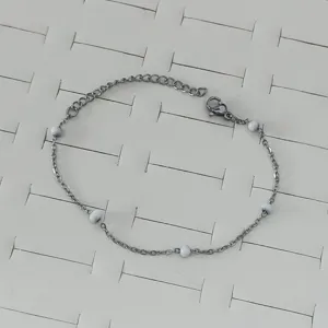 Macro detail shot of a stainless steel chain bracelet with marbled white beads on white tray