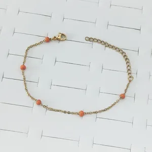 Close-up view of a minimalist gold stainless steel bracelet with vibrant orange beads.