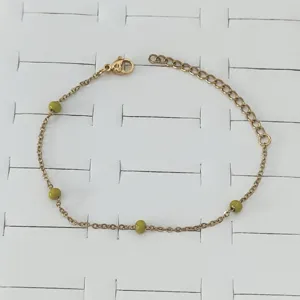 Close-up of gold stainless steel chain bracelet featuring small green enamel beads