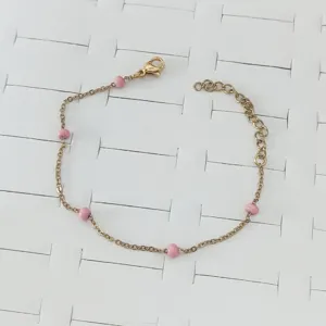 Detailed view of a dainty gold stainless steel bracelet with small pink enamel beads